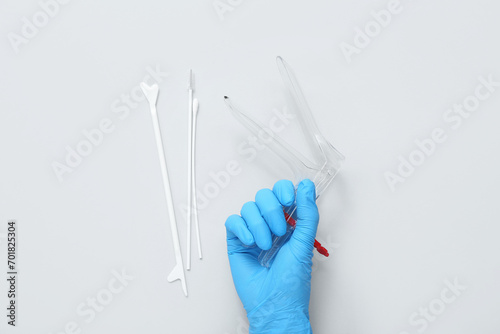 Hand in medical glove, with gynecological speculum and pap smear test tools on light background photo