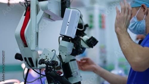 Medic stands near the microscope preparing it for usage at operation. Advanced equipment in neurosurgery. photo