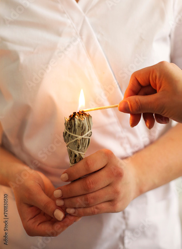 Spa worker in white medical uniform holding and lighting herbal incense photo