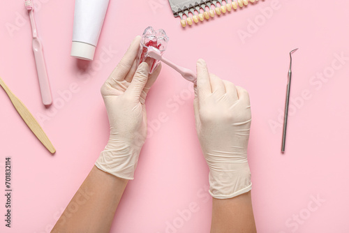 Dentist with plastic tooth and brush on pink background, top view photo