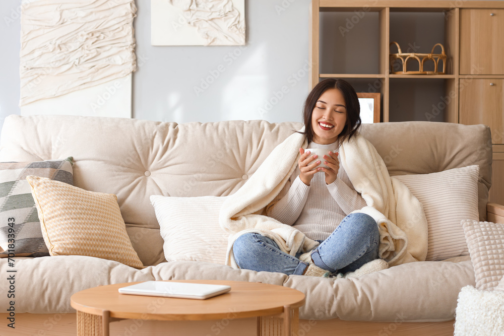 Young Asian woman with warm plaid drinking tea at home