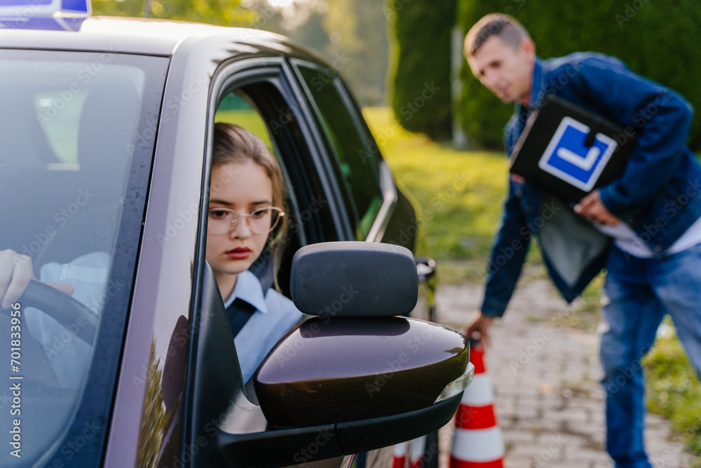 Naklejka premium Driving Test. Training parking. Cones for the examination, driving school concept. Alert nervous young teen girl student driver taking driving education lesson test from male instructor.