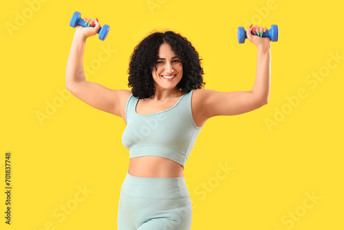 Sporty adult woman with dumbbells on yellow background photo