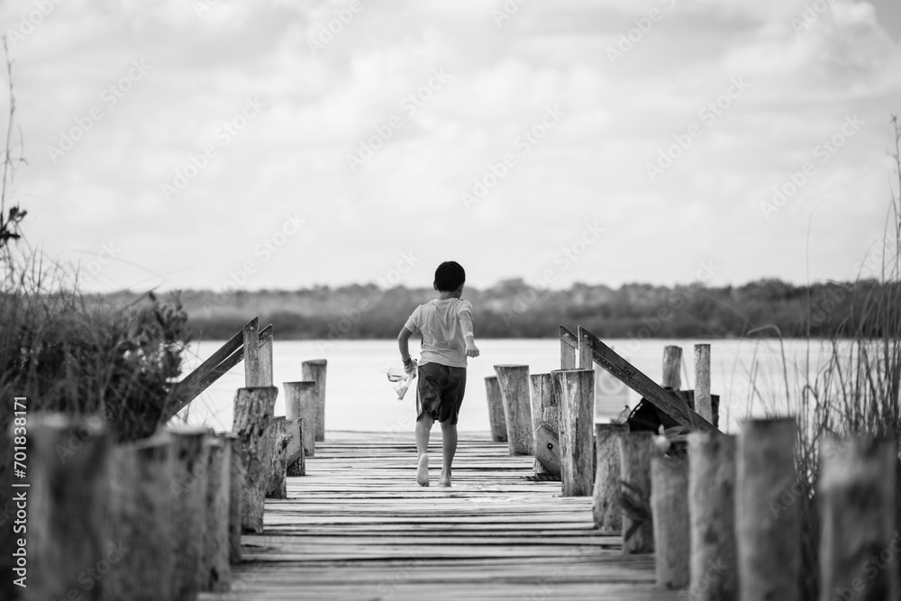 Obraz premium A boy running on a wooden bridge over a lake, black and white.