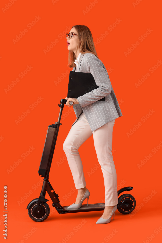 Portrait of young businesswoman with kick scooter and clipboard on orange background Portrait of young businesswoman with kick scooter and clipboard on orange background