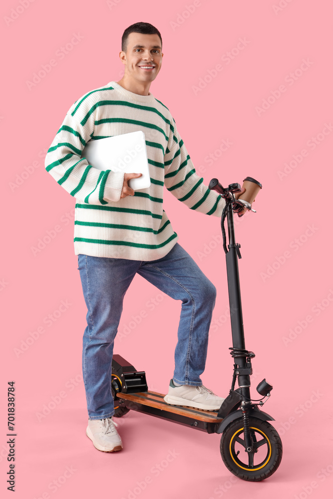 Young man with laptop and kick scooter on pink background