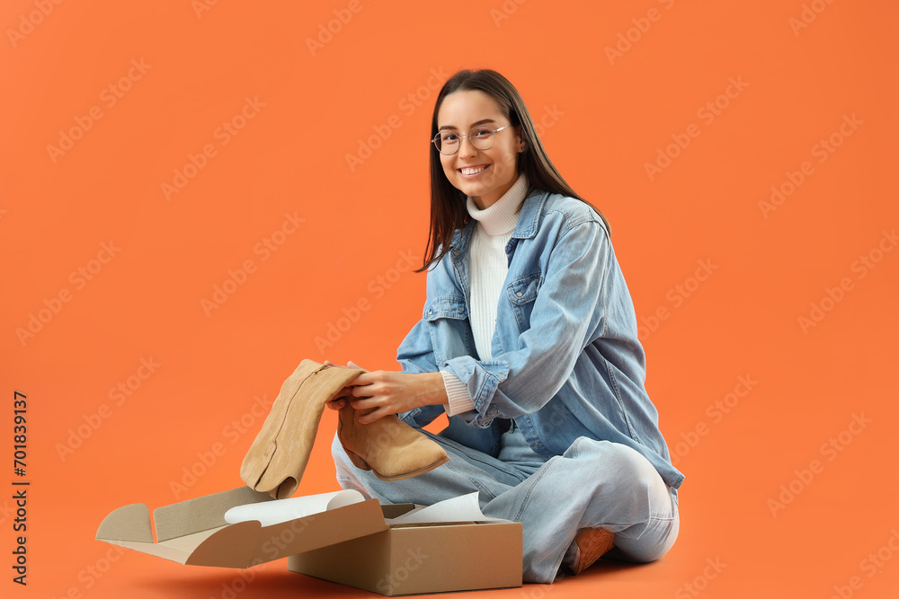Female seller with boots in box on orange background Female seller with boots in box on orange background