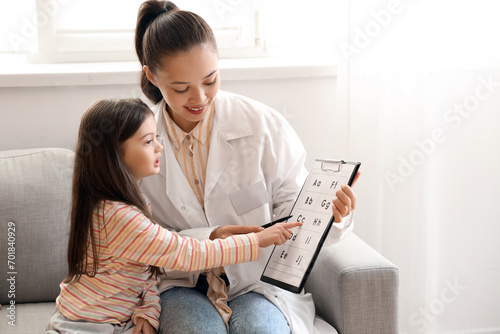 Female Asian speech therapist showing clipboard with letters to little girl in office photo