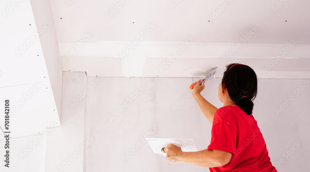 Hands of worker plaster ceiling with white putty and trowel, woman at work by plastering a ceiling of construction site.Home renovation and building new house.