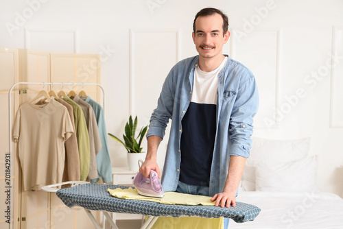Young man ironing t-shirt o...