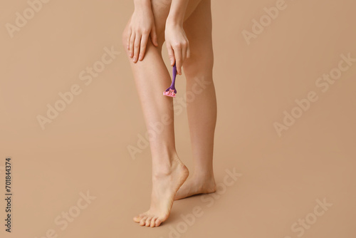 Beautiful young woman with razor shaving legs on brown background  closeup