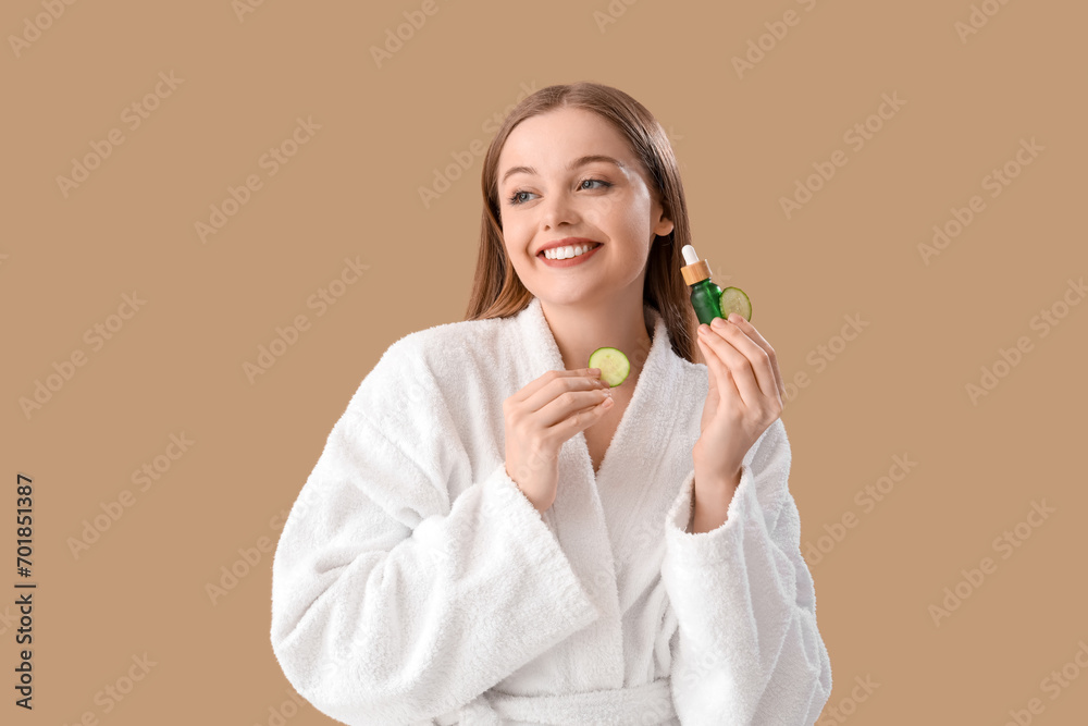 Young woman in bathrobe with cucumber slices and serum on beige background Young woman in bathrobe with cucumber slices and serum on beige background