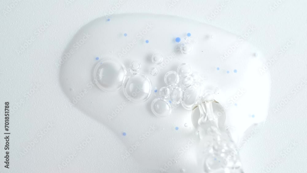 Liquid fluid transparent gel or serum with blue granules in pipette drips on a white surface. Dropper for cosmetic fluid with bubbles from above. Liquid fluid transparent gel or serum with blue granules in pipette drips on a white surface. Dropper for cosmetic fluid with bubbles from above.