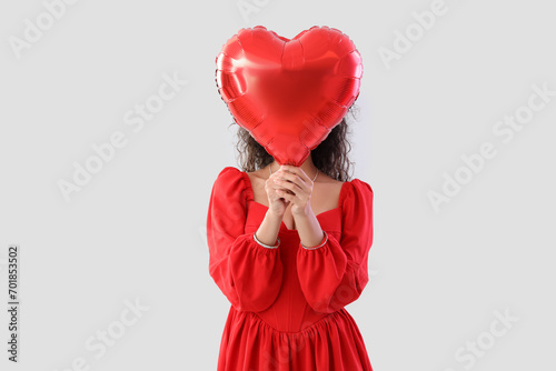 Young African-American woman with heart-shaped balloon on light background. Valentine's Day celebration