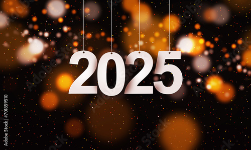Happy New Year 2025 with small glitters sprinkling down. Hanging white paper cut number with festive confetti on an orange golden blurry bokeh background.