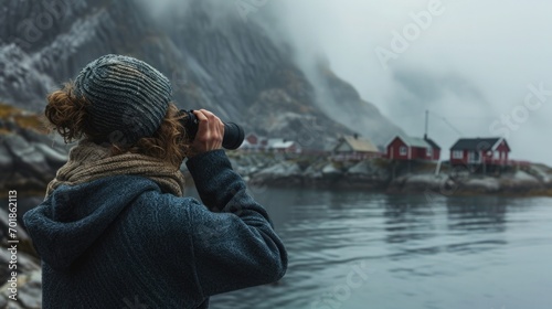 Seaside Town overlooking a foggy fjord, a small Scandinavian fishing village. A woman in a wool sweater looks binoculars. photo