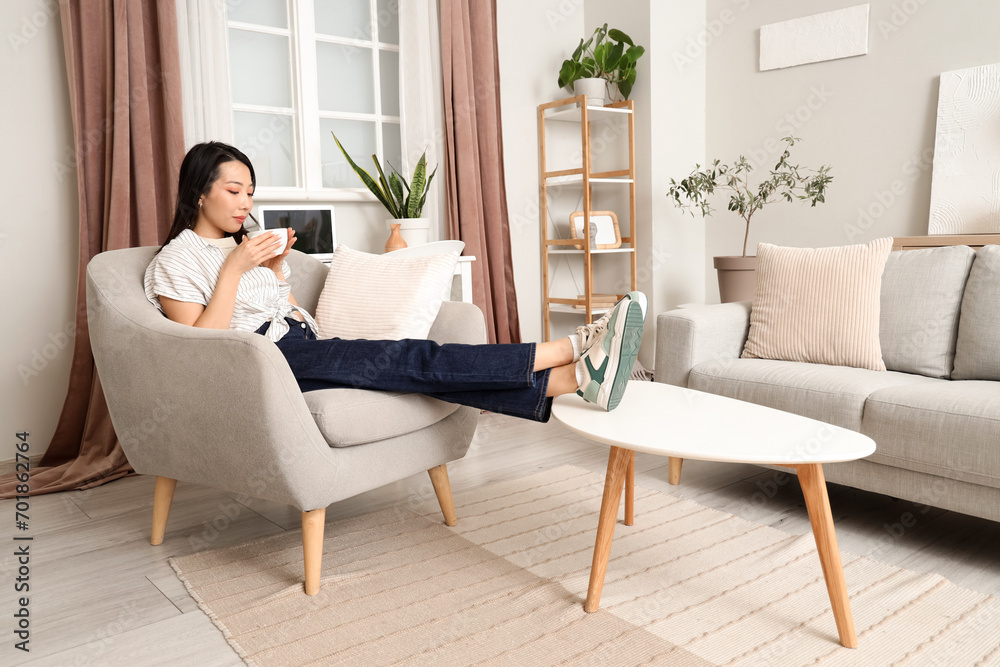 Young Asian woman drinking coffee in armchair at home Young Asian woman drinking coffee in armchair at home