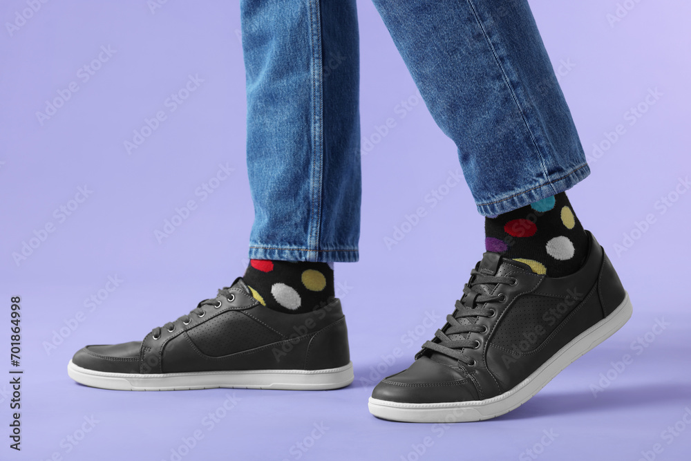 Man in stylish colorful socks, sneakers and jeans on violet background, closeup Man in stylish colorful socks, sneakers and jeans on violet background, closeup