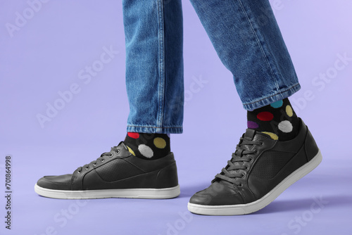 Man in stylish colorful socks, sneakers and jeans on violet background, closeup