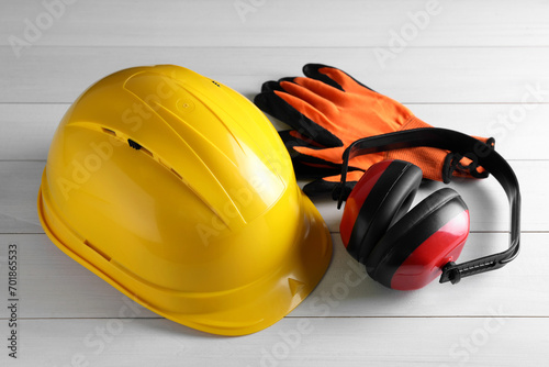 Hard hat, earmuffs and gloves on white wooden table. Safety equipment photo