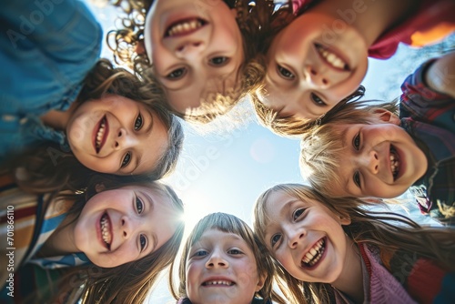 Group of joyful children forming a circle and looking down at the camera, with sunlight filtering through on a bright day