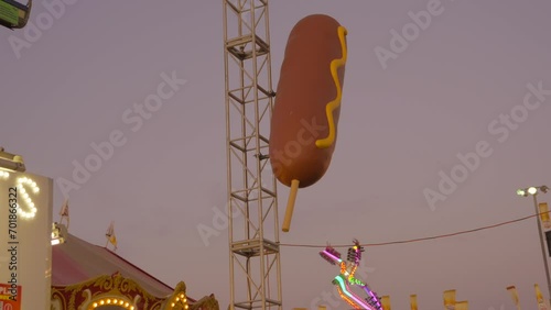 This video shows a giant corndog statue at a state fair in evening lighting.