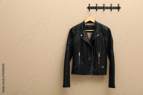 Hanger with black leather jacket on beige wall, space for text