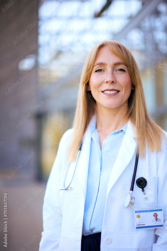 Portrait Of Smiling Female Doctor Wearing White Coat Standing Outside Modern Hospital Building Portrait Of Smiling Female Doctor Wearing White Coat Standing Outside Modern Hospital Building