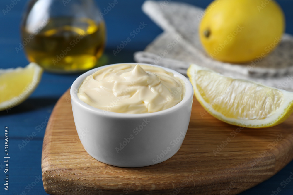 Tasty mayonnaise in bowl and lemon wedge on blue table, closeup Tasty mayonnaise in bowl and lemon wedge on blue table, closeup