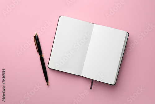 Open notebook with blank pages and pen on light pink background, top view. Space for text photo