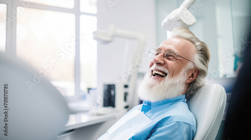 Elderly male patient with white hair is smiling and sitting in a dental chair photo