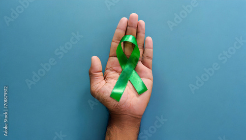 Green ribbon on blue background. Cancer Awareness Month. Copy space.