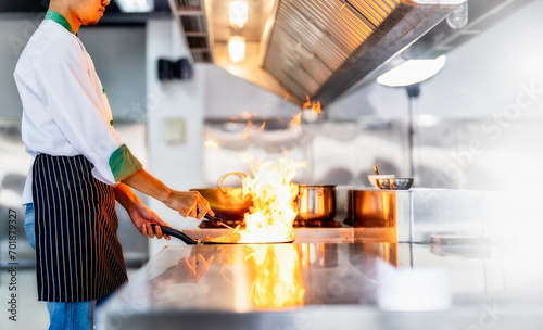 Chef in restaurant kitchen at stove and pan cooking flambe on food photo