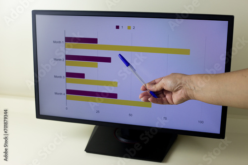 Woman hand holds a pen and points to a bar chart with colorful stripes on a computer screen