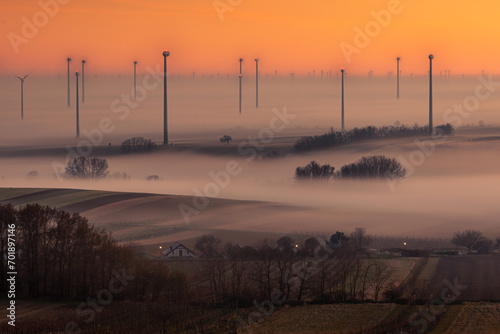 Wind power plants under in Berg, Burgenland, Austria. Foggy weather after sunset. Stunning panorama of wind turbines. Renewable energy. Renewable energy source.