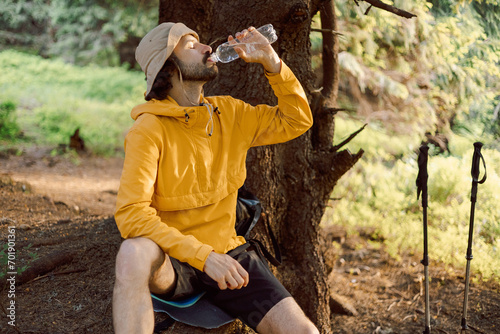 photo of a thirsty man traveling in the Carpathian forested mountains and drinking cool water from a bottle in the shade of a tree with great thirst © Максим Галінский