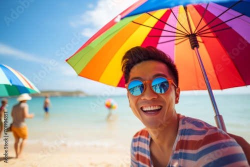 happy asian man on the beach in summer against the background of the sea or ocean and colorful umbrella