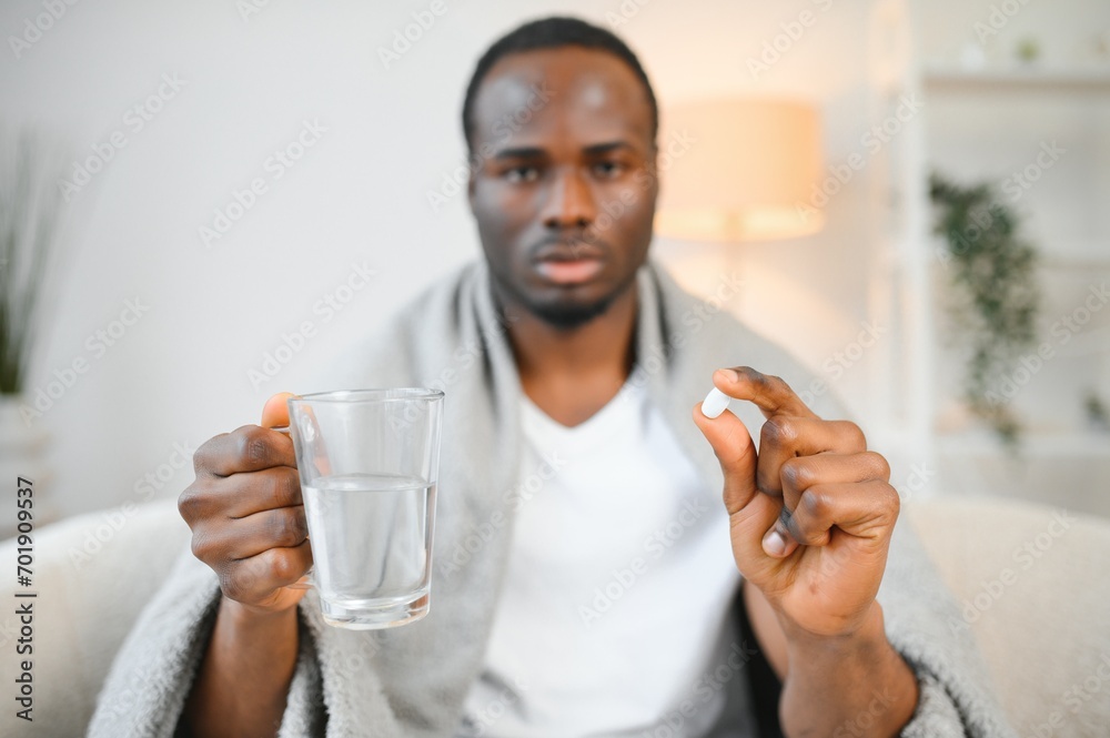 Serious young black bearded male sitting on bed in bedroom, hold glass of water and tablet on white wall background Serious young black bearded male sitting on bed in bedroom, hold glass of water and tablet on white wall background