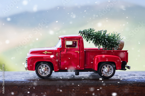 Red retro small car carrying christmas tree in the mountain in snowfall. Winter holiday concept
