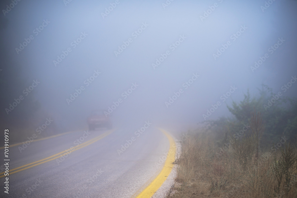 Retro car entering in a fog passing by country mountain road