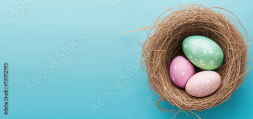 horizontal banner, painted multicolored eggs in a basket, Easter, birds nest, wicker basket on a blue background, place for text