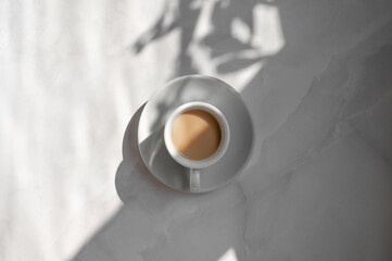 Minimal aesthetic lifestyle coffee concept, saucer and cup with milky coffee on marble gray table background with natural geometric sunlight shadow, good morning business branding backdrop