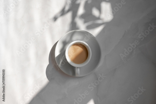 Minimal aesthetic lifestyle coffee concept, saucer and cup with milky coffee on marble gray table background with natural geometric sunlight shadow, good morning business branding backdrop