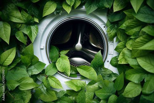 Washing machine with green leaves in it. Eco cleaning, eco friendly washing concept. Environmentally friendly bio natural home cleaning. Plants near modern washing machine. Spring cleaning theme.