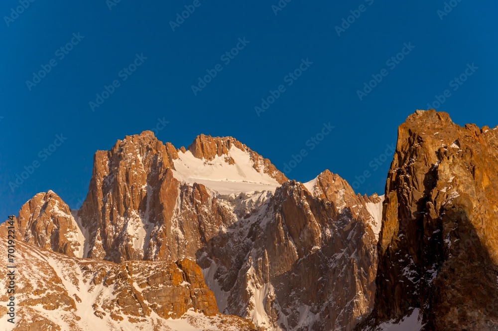 Korona Peak, with rugged, snow-laced cliffs, towers under the blue sky, a beacon for climbers worldwide
