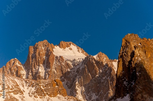 Korona Peak, with rugged, snow-laced cliffs, towers under the blue sky, a beacon for climbers worldwide