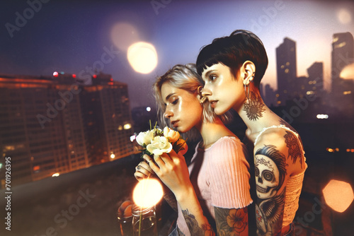 A young female couple in a romantic moment on a rooftop. Tattooed punk style, set against the backdrop of a cityscape on a summer night. 