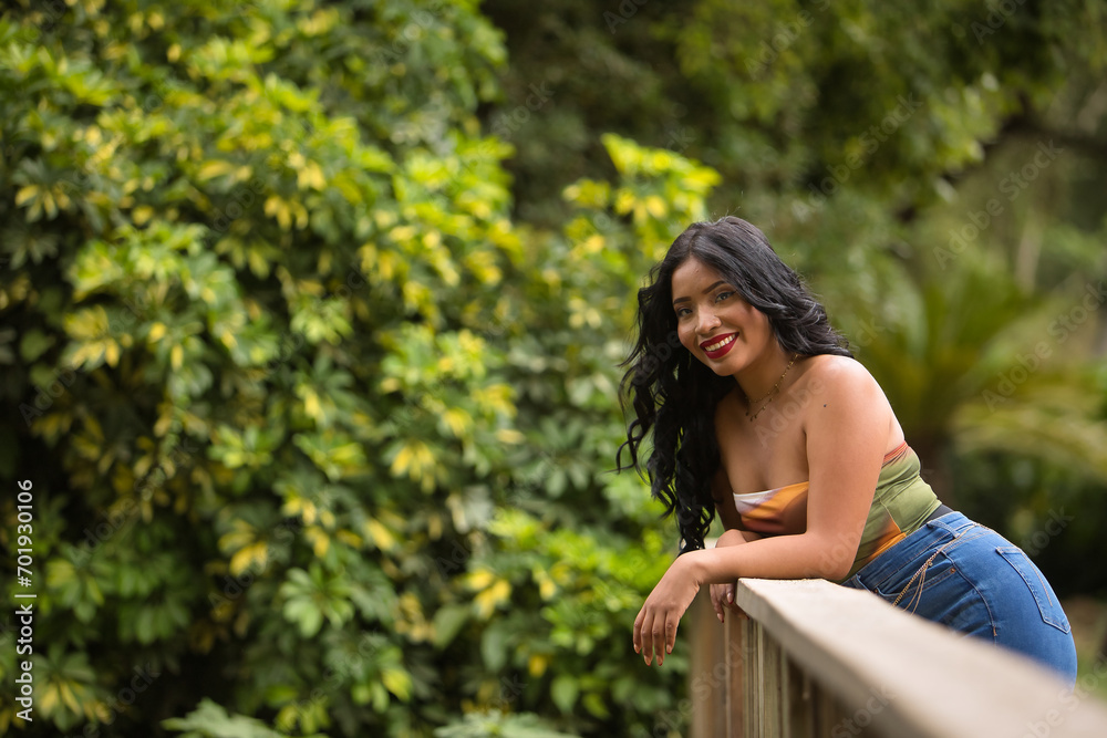 South American woman, young, beautiful, brunette, with colorful top and jeans leaning on a wooden railing looking at the camera smiling and happy. Concept of beauty, trend, ethnicity, diversity. South American woman, young, beautiful, brunette, with colorful top and jeans leaning on a wooden railing looking at the camera smiling and happy. Concept of beauty, trend, ethnicity, diversity.