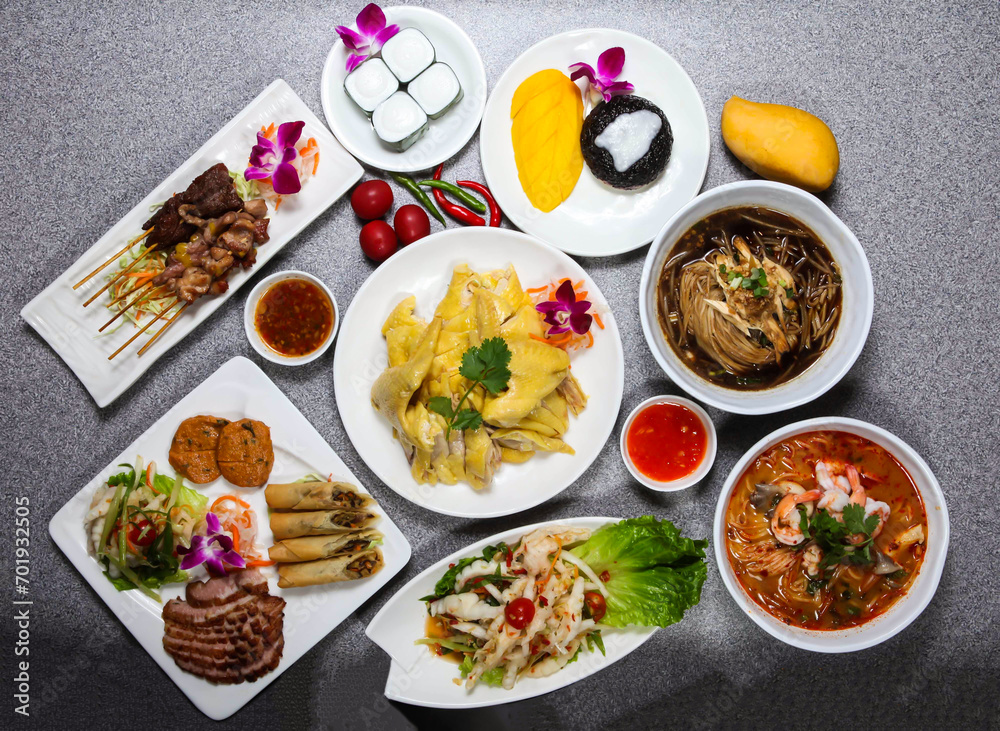 Assorted thai food with grilled pork neck, fish cake, spring roll, chicken feet, beef and chicken satay, sago cake, sticky rice with mango served isolated on background top view of hong kong food