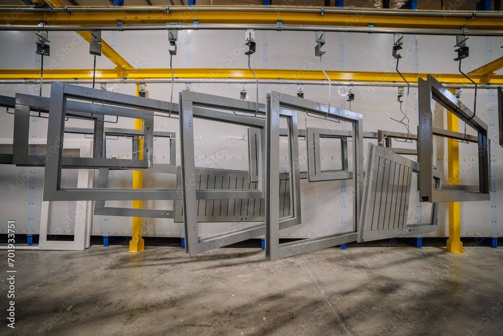 an industrial setting with several large gray wooden window frames or structures hanging from an overhead conveyor system. an industrial setting with several large gray wooden window frames or structures hanging from an overhead conveyor system.